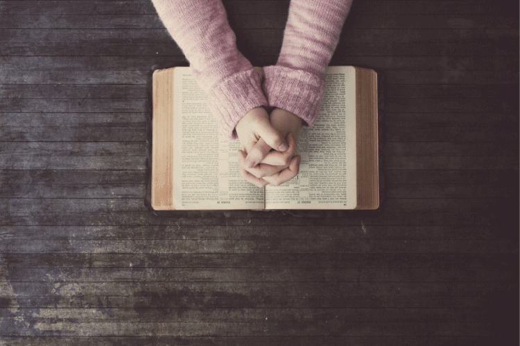 woman's hands folded over a Bible
