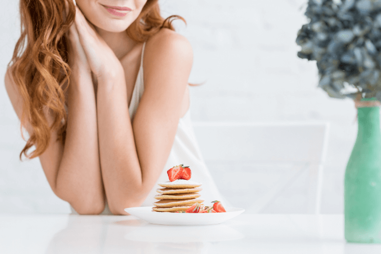 photo of woman looking at pancakes and strawberries on a plate