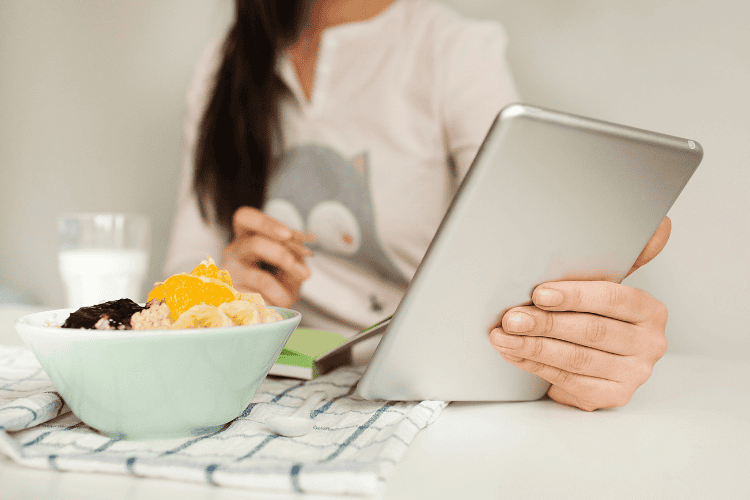 woman looking at her tablet while eating a meal