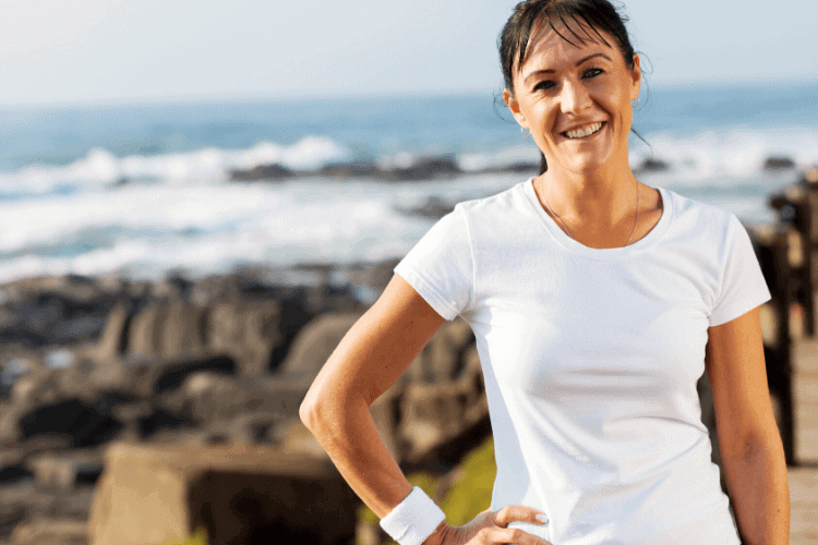 woman smiling standing on the beach after exercising 